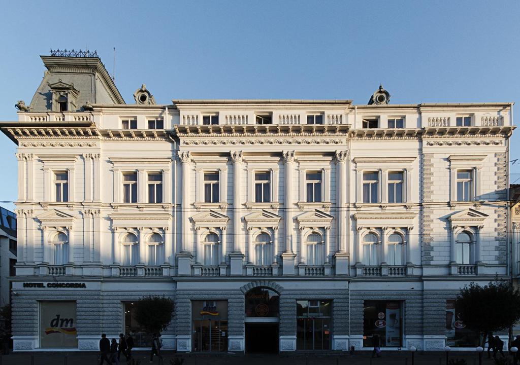 un gran edificio blanco con gente delante de él en Hotel Concordia, en Târgu Mureș