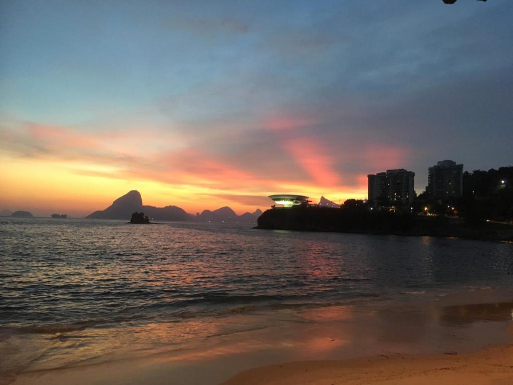 a sunset on the beach with mountains in the background at Apartamento Icarai Praia in Niterói