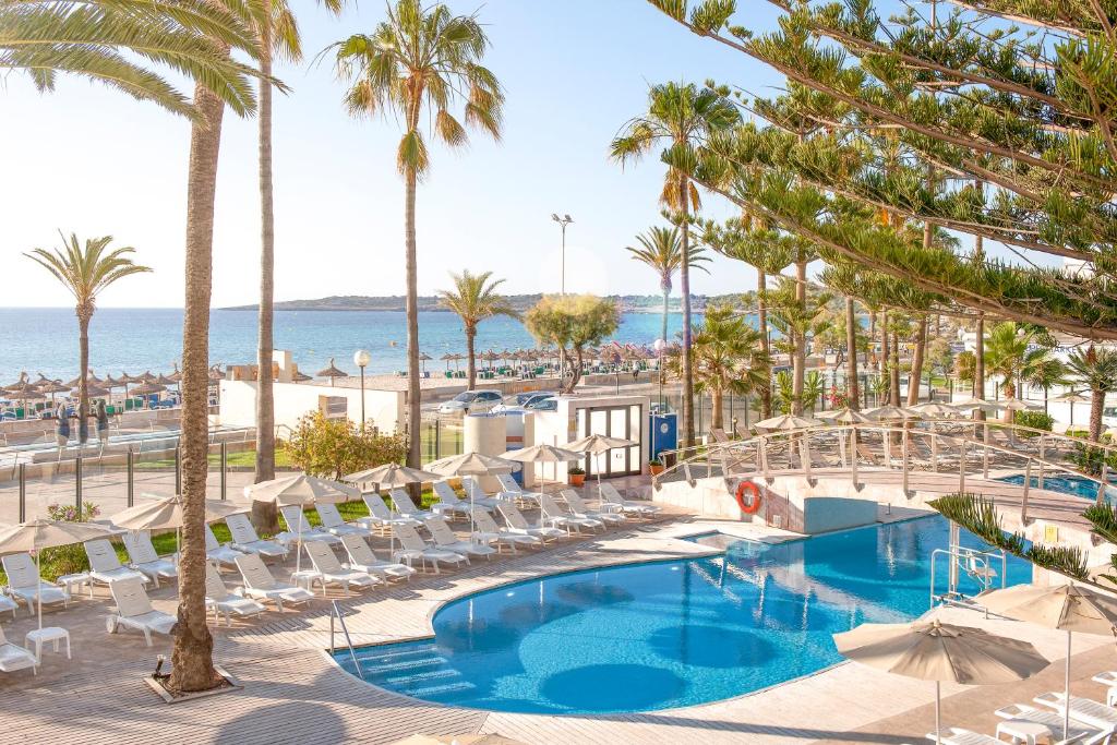 uma imagem de uma piscina de resort com palmeiras e o oceano em CM Playa del Moro em Cala Millor