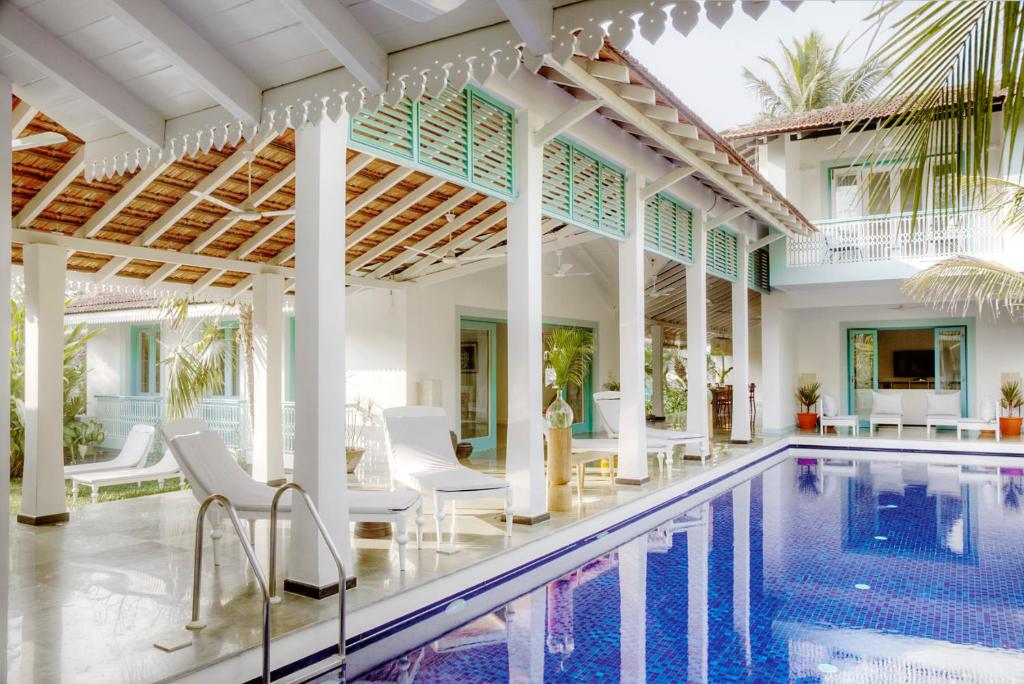 an indoor swimming pool with white chairs and a pool house at Assagao Bay by the Rose Nomad in Assagao