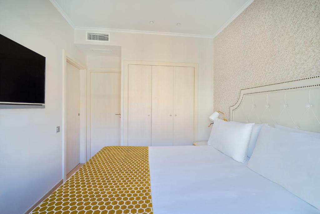 a bedroom with a bed with a white bedspread and a television at Tandem Soho Suites in Málaga