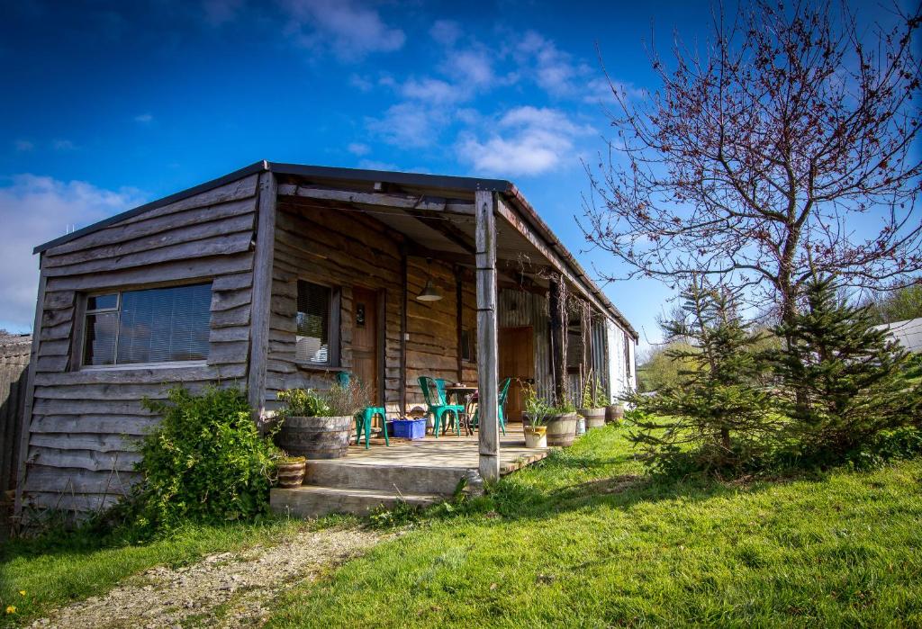 una pequeña casa de madera con porche y algunas sillas en Ceridwen Glamping, double decker bus and Yurts en Llandysul