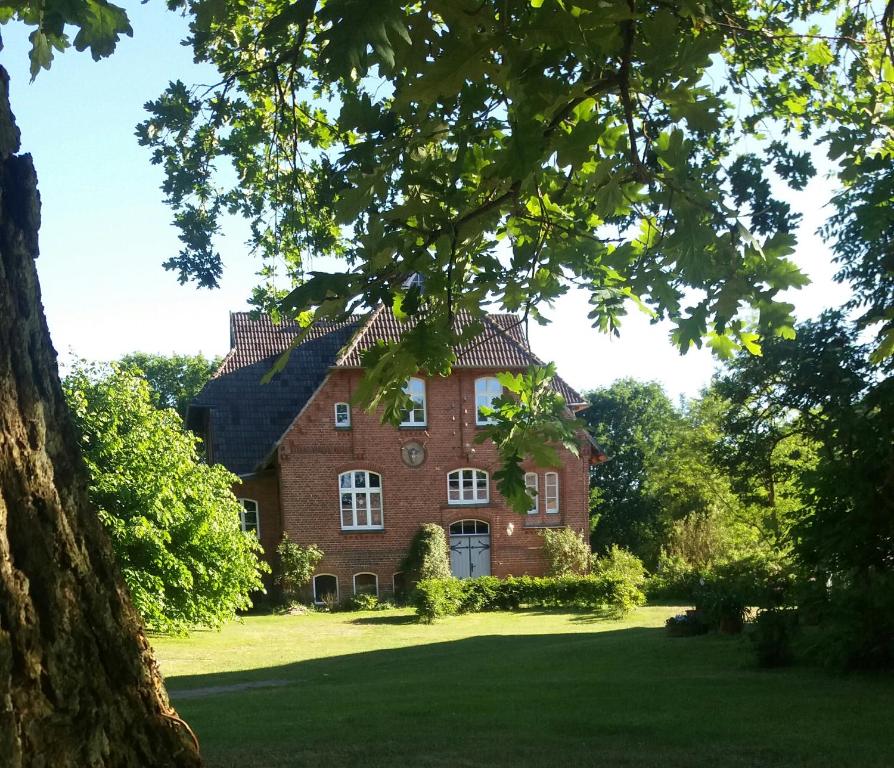 a large red brick house with a tree in the foreground at Ferienwohnung ehemalige Revierförsterei "Morgensünn" in Kuhstorf