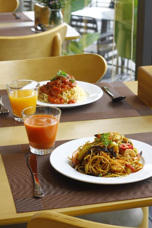 Two plated pasta dishes with orange drinks at a bright dining table.
