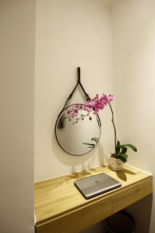 A compact wooden desk with a laptop, round mirror, and orchid decoration.