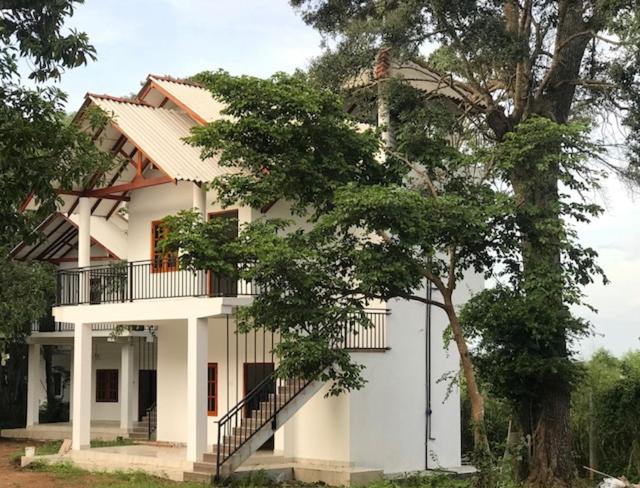 a white house with a balcony and a tree at Andarawewa Nature Resort in Anuradhapura