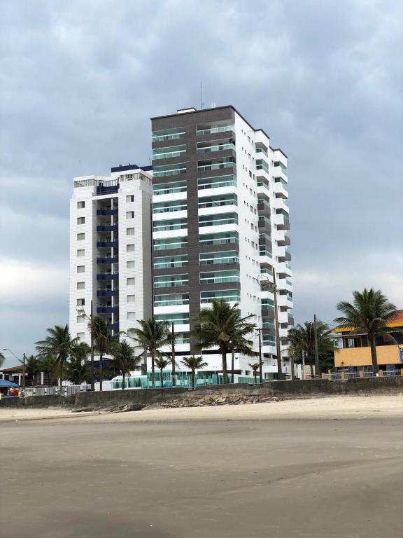 a tall white building with palm trees in front of it at Edifício Copacabana frente para mar in Mongaguá