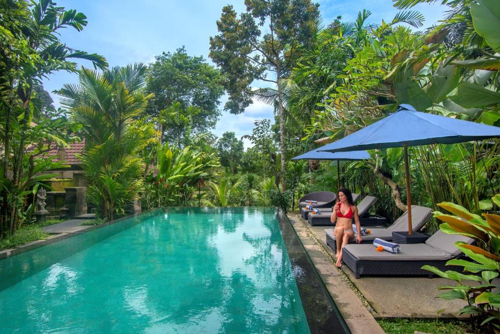 a woman sitting on a chair next to a swimming pool at Alam Dania Cottage in Ubud