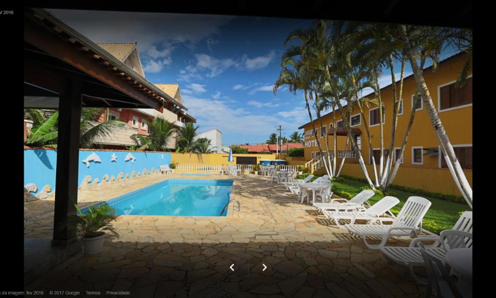 a swimming pool with white chairs and a resort at Hotel Xapuri in Peruíbe