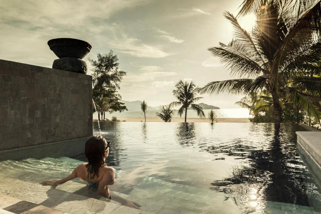 a woman sitting in a swimming pool next to a body of water at Four Seasons Resort Langkawi in Tanjung Rhu