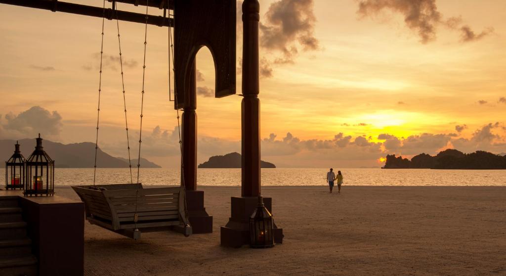 a bench on the beach with a sunset in the background at Four Seasons Resort Langkawi in Tanjung Rhu
