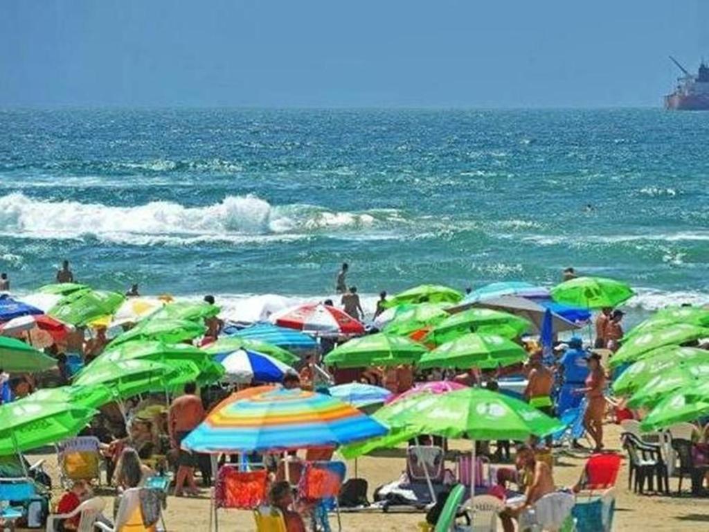 um grupo de pessoas em uma praia com guarda-sóis em Casa da Felicidade em Tramandaí