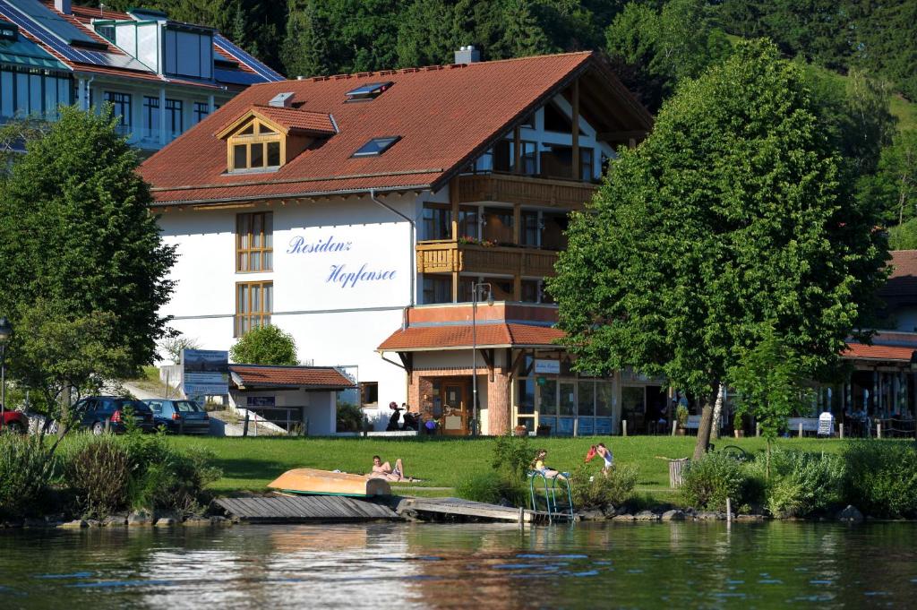 a building with people sitting on the grass near a river at Residenz Hopfensee in Füssen