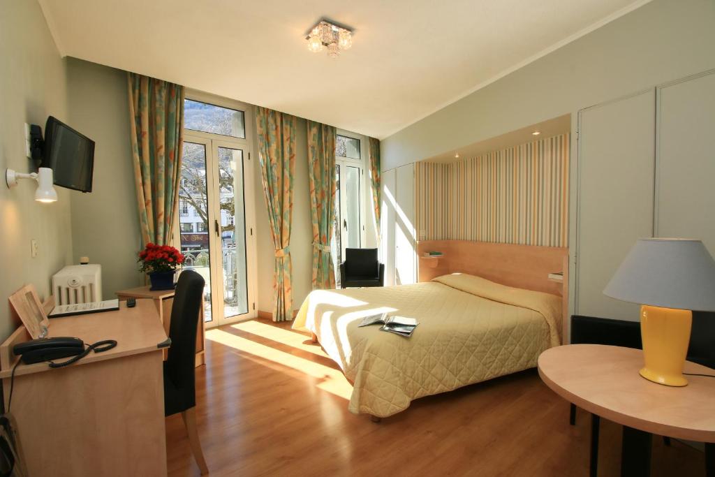 a hotel room with a bed and a desk and a window at Hôtel Panoramic in Luchon