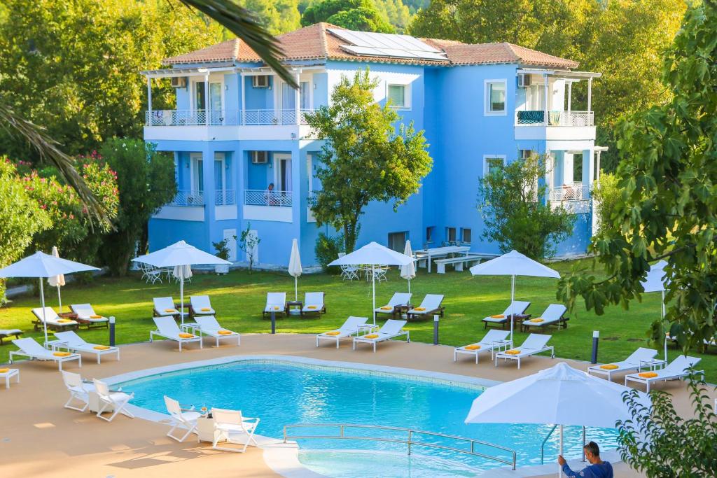 a pool in front of a blue building with chairs and umbrellas at Mandraki Village Boutique Hotel in Koukounaries