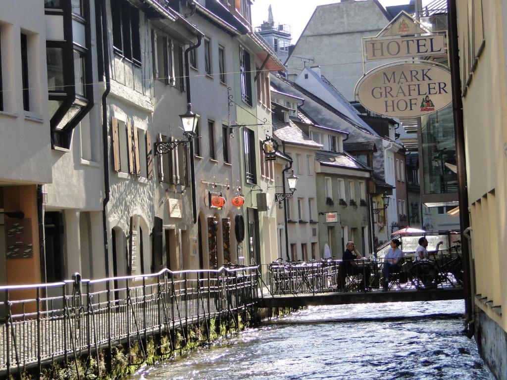 un canal en una ciudad con edificios y gente sentada en sillas en StayInn Apartments City Center en Freiburg im Breisgau