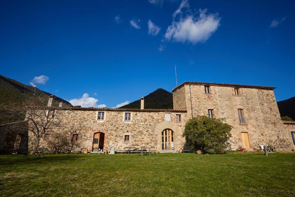 um grande edifício de pedra com um campo de relva em frente em Masia de Vallforners em Tagamanent