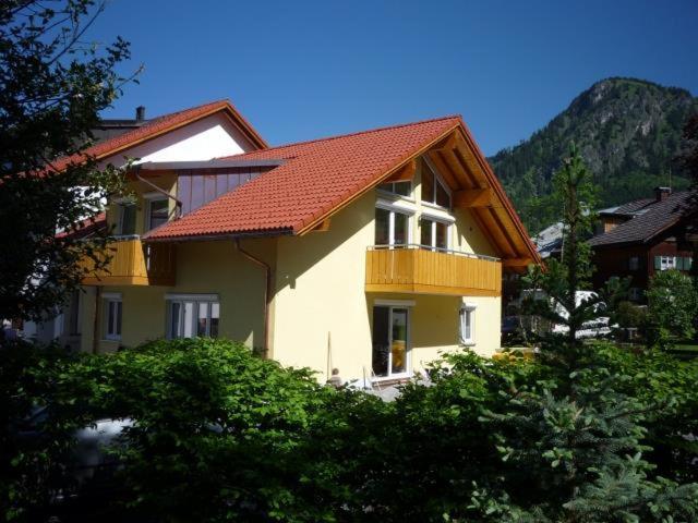 una casa gialla con un tetto rosso e alcuni alberi di Ferienwohnung Iselerblick a Bad Hindelang