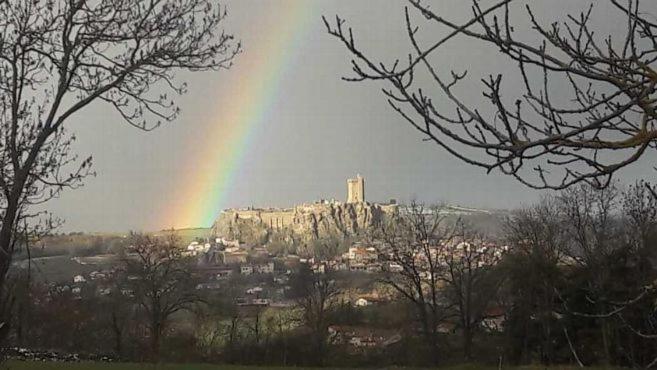 Ein Regenbogen am Himmel über einer Stadt mit einem Schloss in der Unterkunft La maison D'Orée in Polignac
