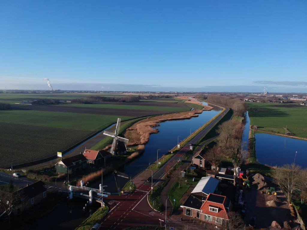 uma vista aérea de um rio com um moinho de vento e casas em VAKANTIEHUISJE Daar bij de Molen tussen Alkmaar en Hoorn em Oterleek