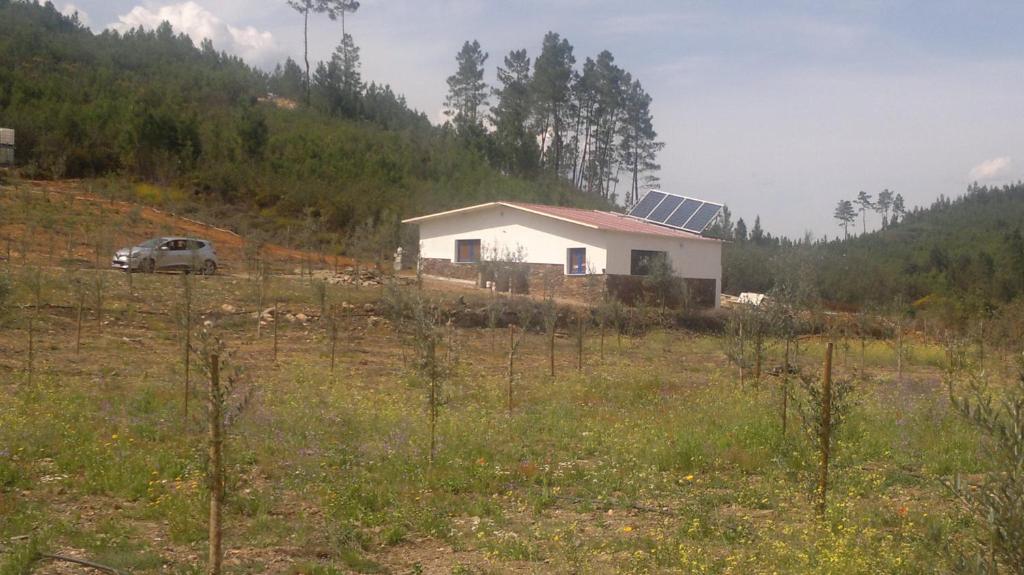 una casa en un campo con un coche delante en REFÚGIO DO RAPOSO/CASA DA RIBEIRA (AGROTURISMO), en Proença-a-Nova