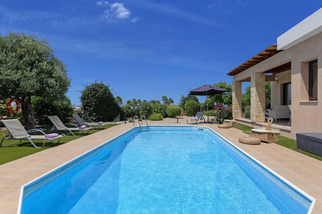 a swimming pool in a yard with chairs and a house at Villa Pashiana in Polis Chrysochous