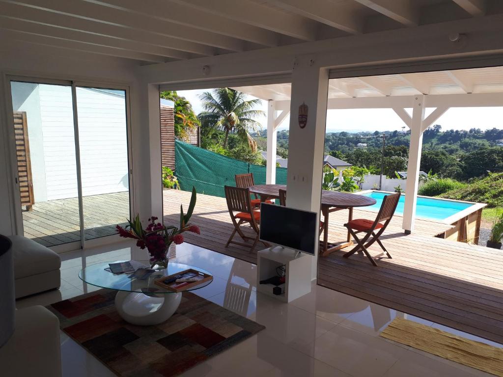 ein Wohnzimmer mit einer Terrasse mit einem Tisch und einem Pool in der Unterkunft EVASION CARAÏBES in Roussel