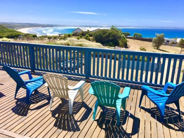 um deque com cadeiras azuis e verdes e a praia em Panoramic Drive Holiday House em Cape Bridgewater