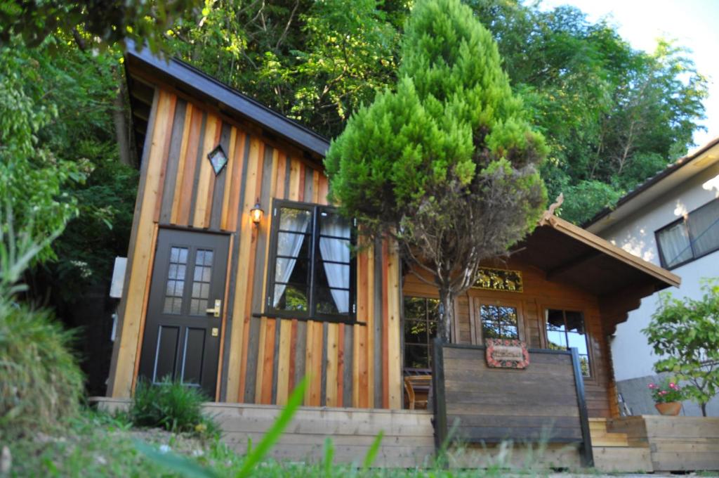 una cabaña de madera con una puerta negra y un árbol en Loft & Log House, en Okayama