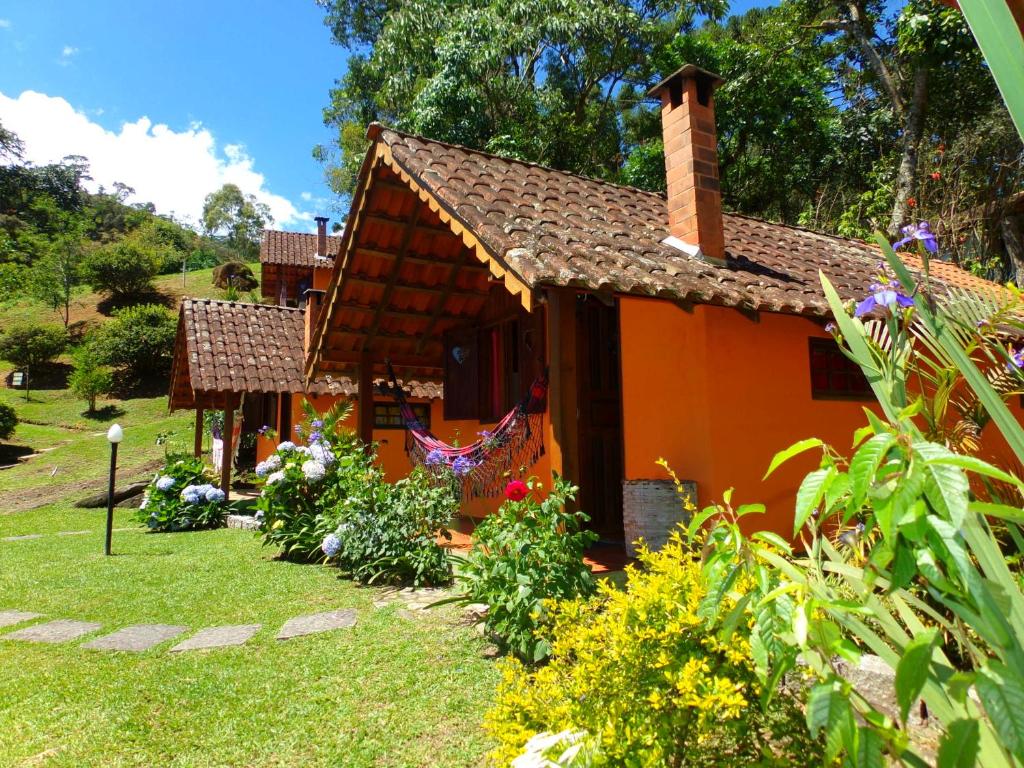 une petite maison orange dans une cour fleurie dans l'établissement Pousada Caminho do Escorrega, à Visconde de Mauá