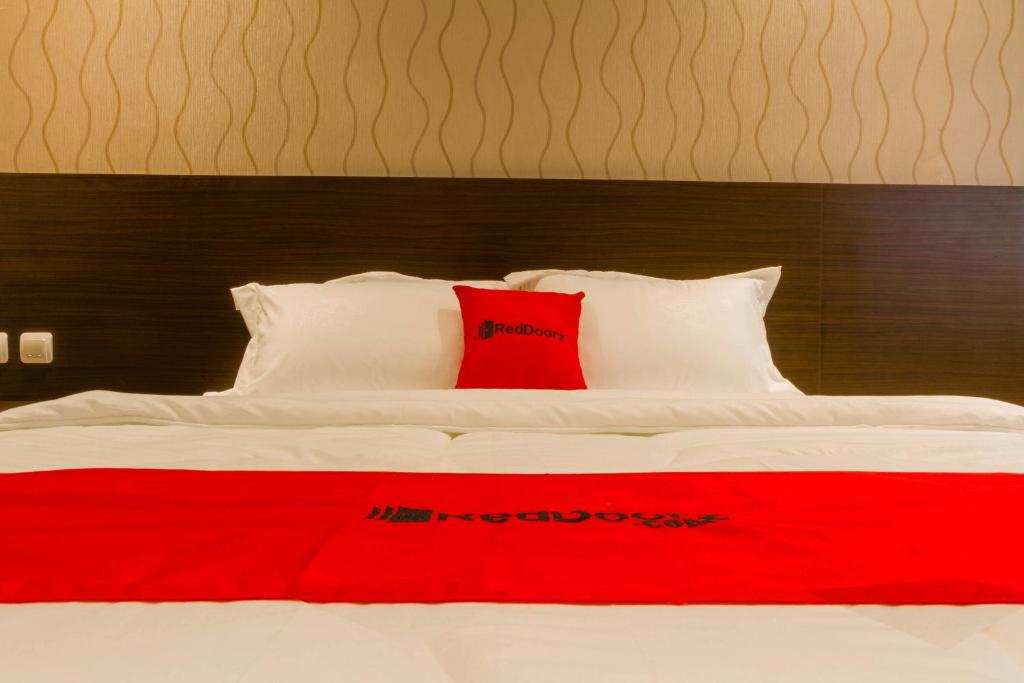 a white bed with a red pillow on it at RedDoorz Plus @ Dipatiukur in Bandung