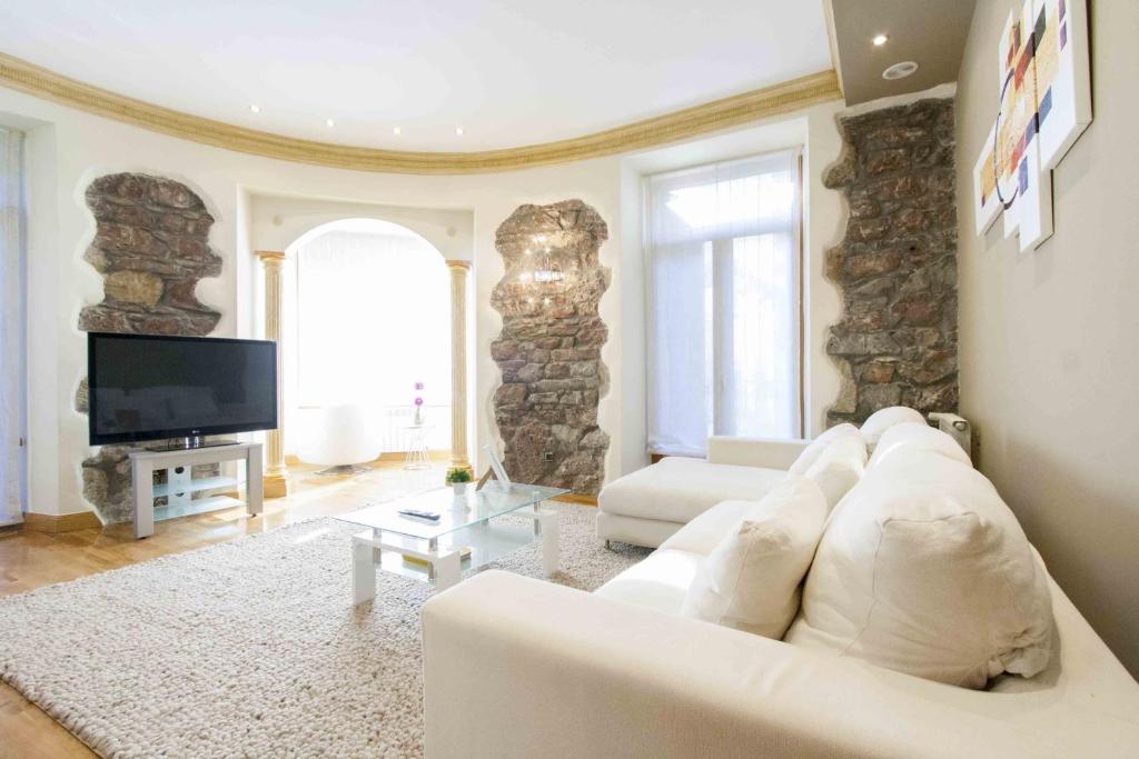 a living room with a white couch and a tv at The Rentals Collection | Camelot in San Sebastián