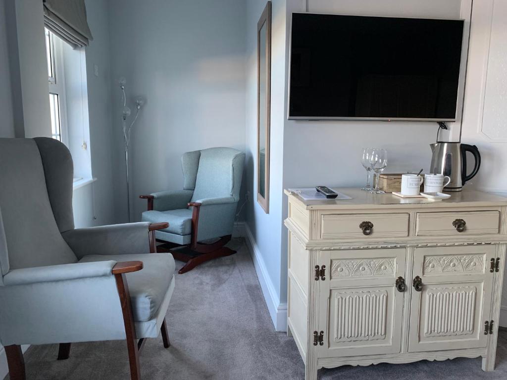 a living room with a tv and two chairs and a dresser at Sunrise Guest House in Bude