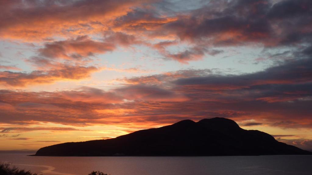 a sunset over a mountain in the ocean with clouds at Kinneil Self Catering in Lamlash