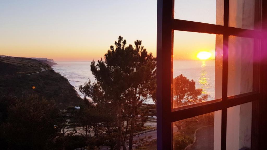 a window view of the ocean with the sunset at Magoito Sea View Apartment in Lisbon