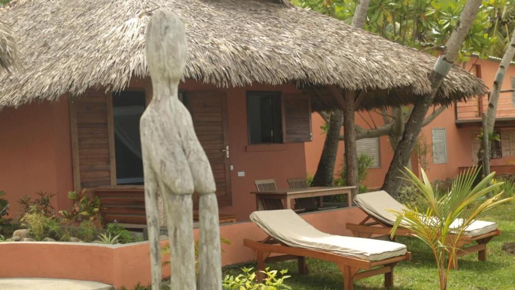 a house with a thatch roof and two chairs and a table at LE TRANSAT in Ambatoloaka