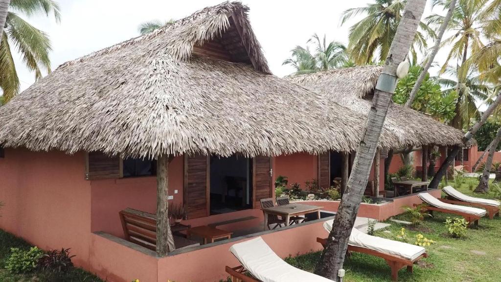 a house with a thatched roof with chairs and a table at LE TRANSAT in Ambatoloaka