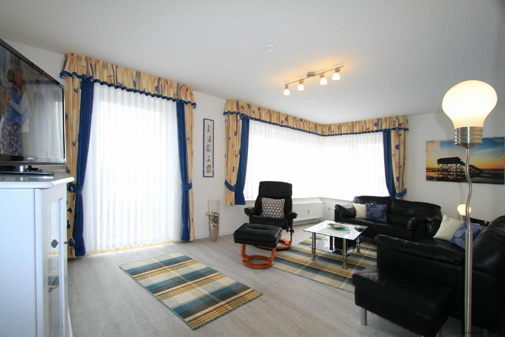 a living room with black furniture and two windows at Haus-am-Boehler-Strand-Wohnung-3 in Süderhöft