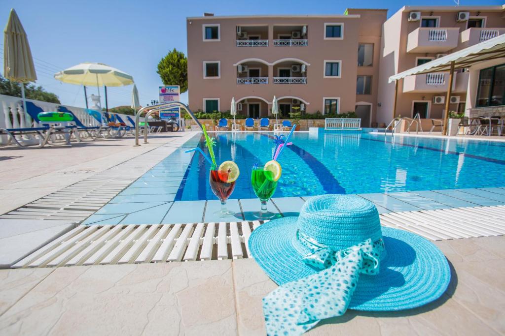ein blauer Hut und zwei Cocktails neben einem Pool in der Unterkunft Kozanos Hotel & Suites in Ammoudi
