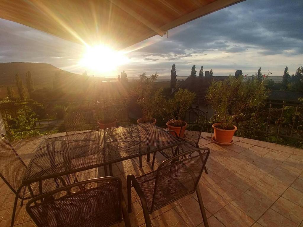 a table and chairs on a patio with the sun at Szigligeti Panoráma Apartmanház in Szigliget