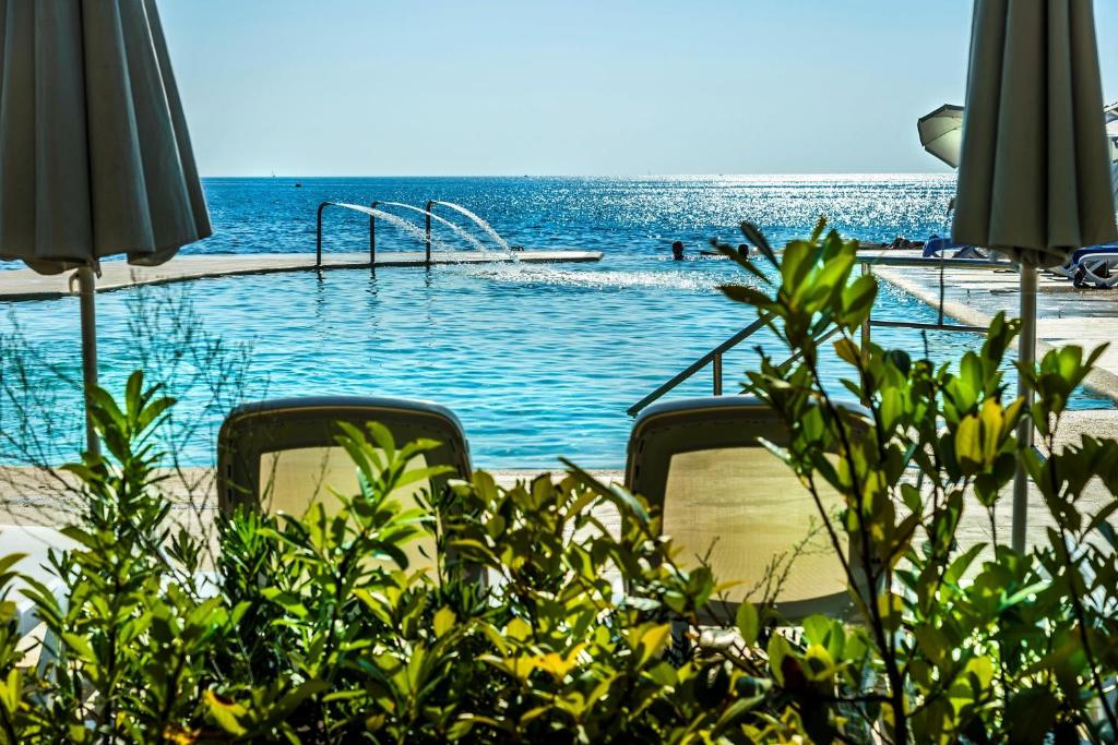 een zwembad naast de oceaan met stoelen en parasols bij Boutique Camping Materada Beach in Poreč