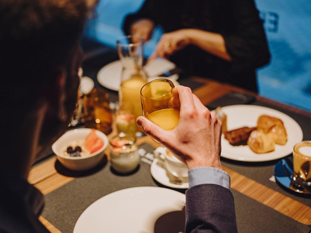 a person holding up a glass of orange juice at a table at El Môderne Hotel in Gijón