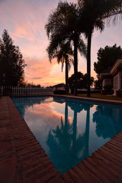 a swimming pool with palm trees and a sunset at Villa Antumalal B&B in Málaga