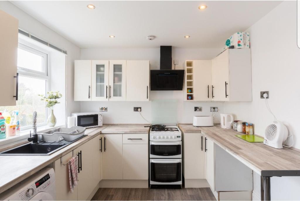 a white kitchen with white cabinets and a sink at Monyhull Homestay - near City centre Kingsheath NIA NEC BHX in Birmingham