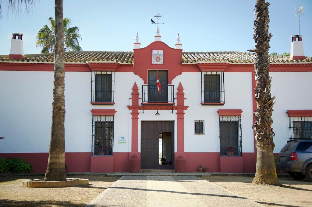 a red and white building with two palm trees at Hacienda de Santa Teresa in Almonte