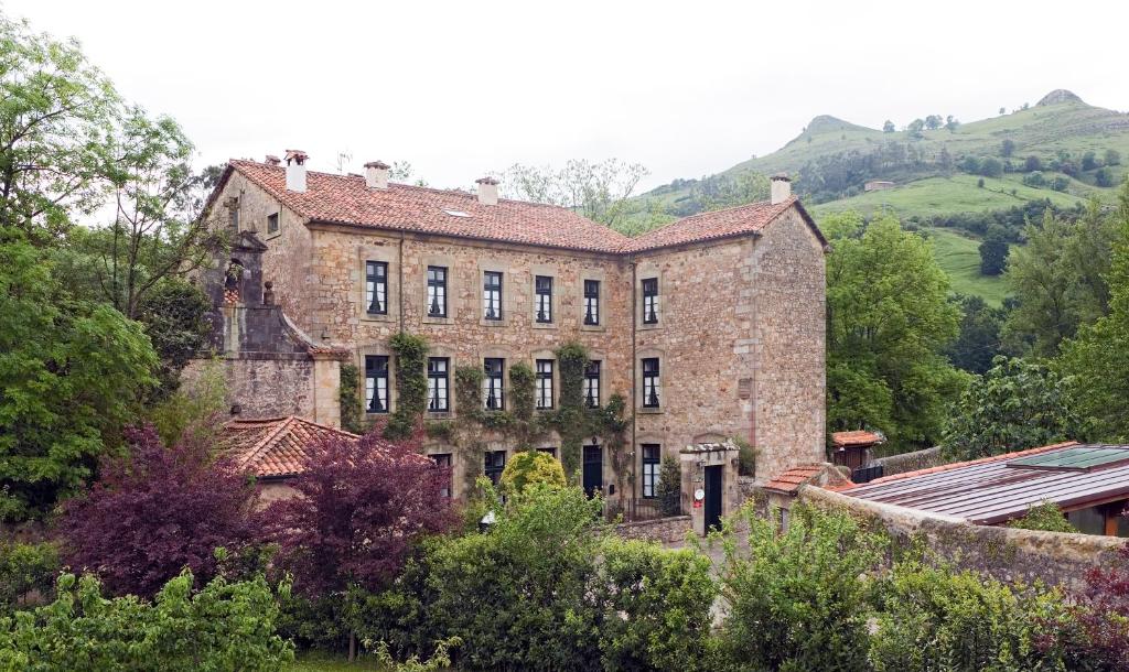 un antiguo edificio de ladrillo con árboles y colinas en el fondo en Hotel Casona El Arral, en Liérganes