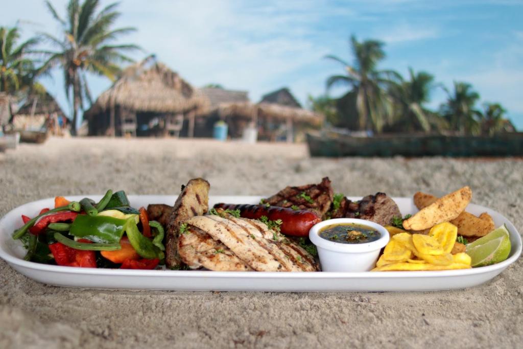 a plate of food with meat and vegetables on the beach at Splash Inn Dive Resort & Villas in West End