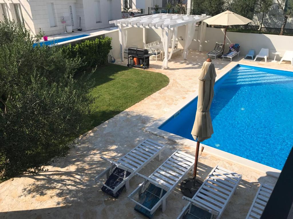 2 sillas de césped y una sombrilla junto a la piscina en Divine Dalmatia Apartments 2, en Tribunj