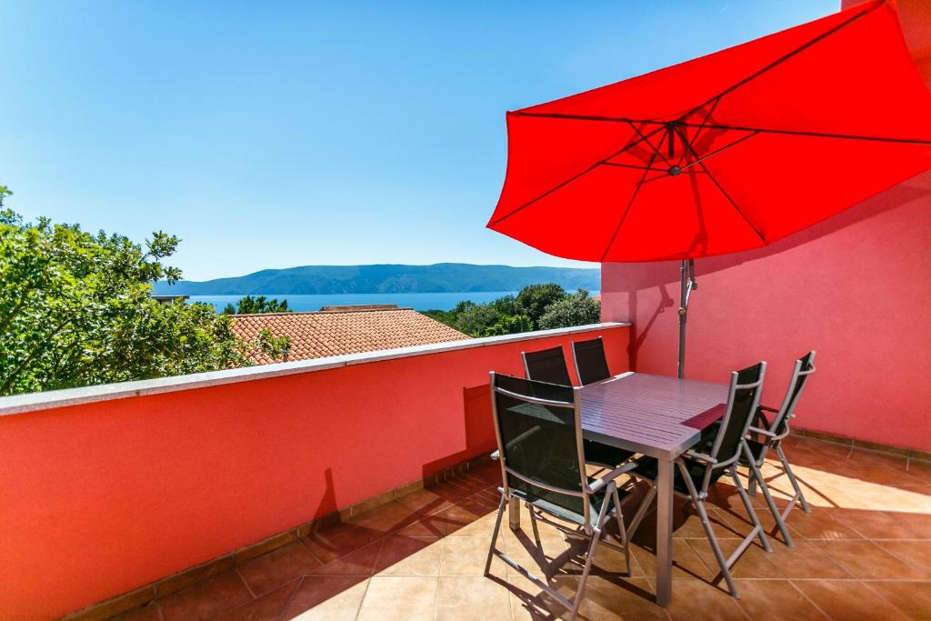 a table and chairs with a red umbrella on a balcony at Apartments Josip in Pinezici