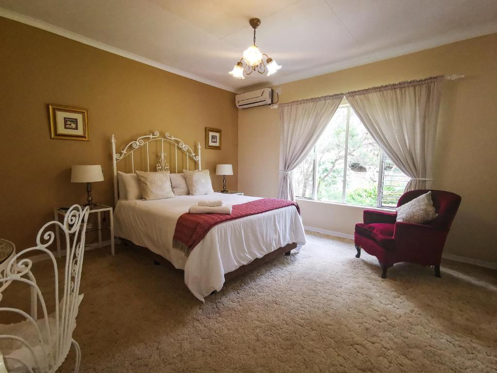 a bedroom with a bed and a chair and a window at Loerie Guesthouse in Hoedspruit